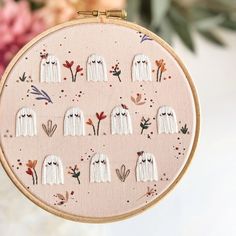 a cross stitch pattern with white ghost heads and flowers in the background on a pink hoop