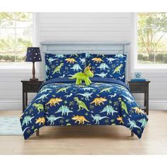 a blue bed with dinosaurs on it and a green stuffed animal sitting on the pillow