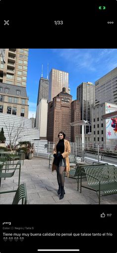 a woman is walking down the sidewalk in front of some benches and tables with tall buildings behind her