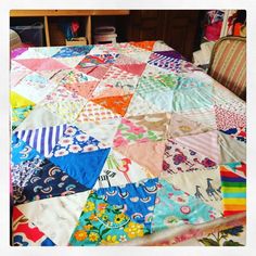 a bed covered in colorful quilts and pillows next to a wooden table with a chair