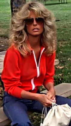 a woman sitting on a park bench wearing sunglasses and holding a bag in her hand