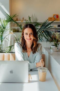 a woman sitting at a table in front of a laptop computer with a cup of coffee