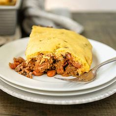 a white plate topped with a piece of meat and vegetable pie next to a fork