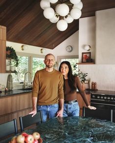 a man and woman standing in a kitchen next to an island with marble counter tops