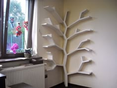 a white tree shaped shelf next to a window in a room with a radiator