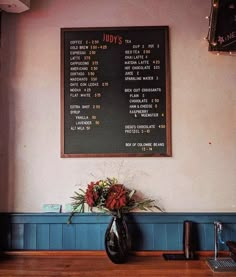 a menu hanging on the wall above a vase with flowers in it and a coffee cup next to it