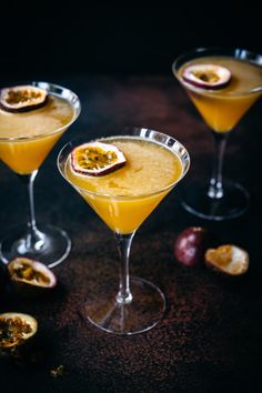 three glasses filled with orange juice and topped with sliced fruit on a black tablecloth