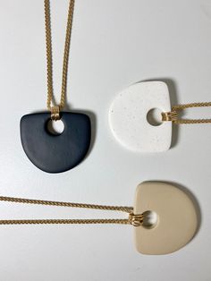 three necklaces with different shapes and colors hanging from gold chains on a white surface