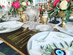 the table is set with plates, silverware and pink flowers in gold vases