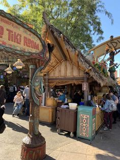 an outdoor food stand with tiki run signs on the roof and people walking around