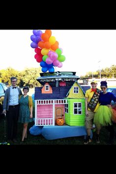 a group of people standing in front of a fake house with balloons on the roof