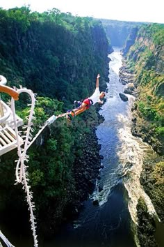 a man is suspended from the side of a bridge over a river in a canyon