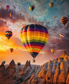 many hot air balloons flying in the sky over some rocks and mountains at sunset or dawn