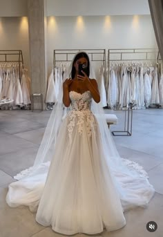 a woman taking a selfie while wearing a wedding dress in a bridal shop