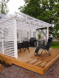 a wooden deck with chairs under a white pergolan