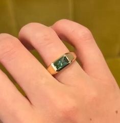 a person's hand with a ring on it that has a green stone in the middle