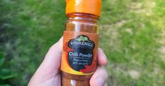 a person holding a jar of chili powder in their left hand and an orange cap on the top