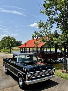 an old black truck parked in front of a wooden bridge