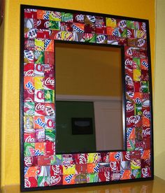 a mirror made out of soda cans on top of a wooden table next to a yellow wall