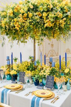 the table is set with yellow flowers and blue place settings for an elegant dinner party