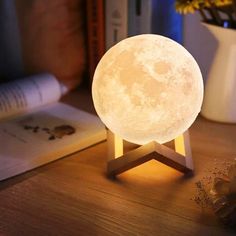 the moon lamp is sitting on top of a wooden table next to an open book