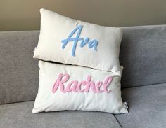 two pillows with embroidered name on them sitting on a couch