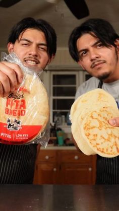 two men in aprons are holding up some bread and one is pointing at the camera