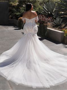 a woman in a white wedding dress is walking down the street with her back to the camera