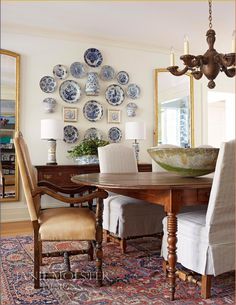 a dining room table with chairs and plates on the wall above it, along with a chandelier