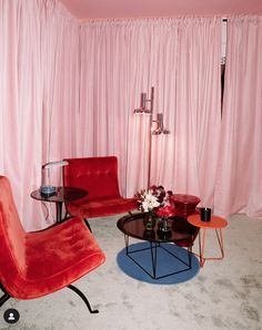 a living room with pink curtains and two red chairs in front of a coffee table