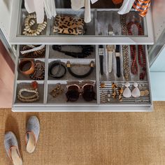 an organized drawer with shoes, jewelry and other items in it on the floor next to a pair of slippers