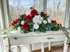 red and white flowers sit on top of an old table in front of a window