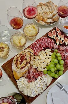 an assortment of cheeses, meats and fruit on a table with wine glasses