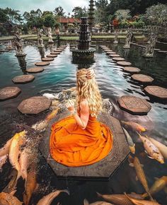 a woman in an orange dress sitting on the edge of a pond surrounded by fish