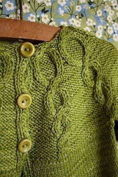 a green knitted sweater hanging on a wooden hanger with flowers in the background