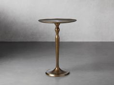 a gold pedestal with a glass top on a gray floor in front of a white wall