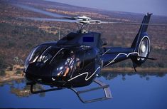 a black helicopter flying over a body of water