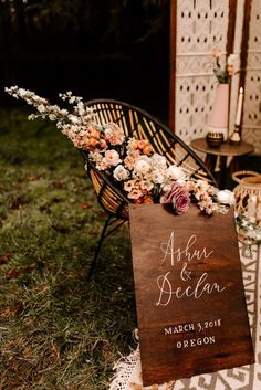 a wooden sign with flowers on it sitting in the grass next to an iron chair