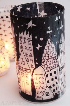 two lit candles are sitting next to each other on a table with paper houses and stars