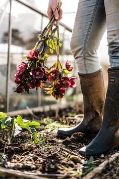 a woman holding flowers in her hands while standing on the ground near a greenhouse door