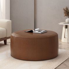 a living room with a white couch and brown ottoman next to a coffee table in front of a window