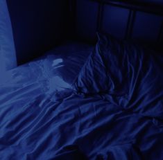 an unmade bed in the dark with blue light shining on it's sheets