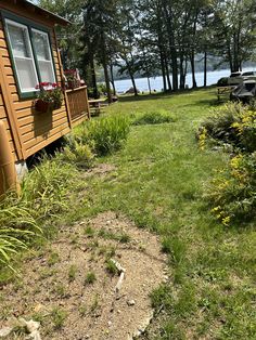 there is a small wooden cabin in the grass by the water with flowers on the window sill