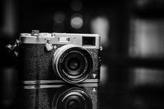 a black and white photo of an old camera on a table with its reflection in the water