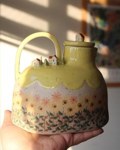 a hand holding a yellow teapot with flowers on it