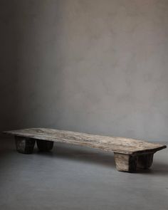 a wooden bench sitting on top of a cement floor next to a white wall with two black wheels