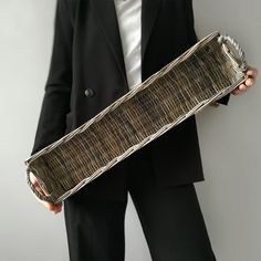 a person in a suit holding a woven piece of luggage with one hand and the other