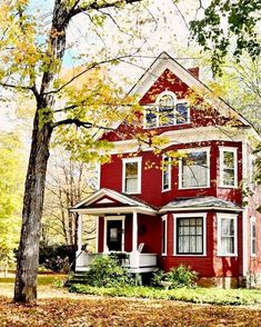 a red house in the fall with leaves on the ground and trees around it,