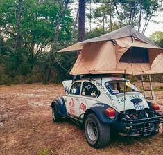 an old vw buggy is parked under a tent in the woods with its roof up