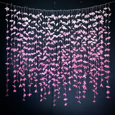 pink and white string art hanging from the ceiling in front of a black wall with birds on it